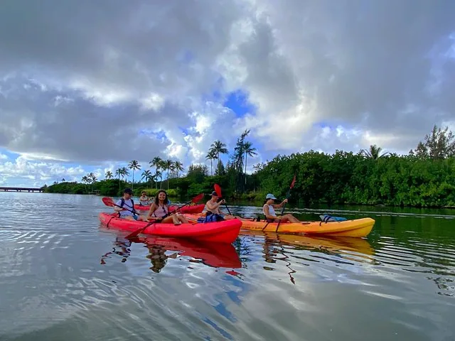 Mehrere Personen paddeln in roten und gelben Kayaks auf einem Fluss.